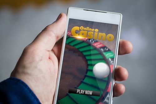 main masculine tenant un smartphone sur lequel apparait un jeu de casino en ligne